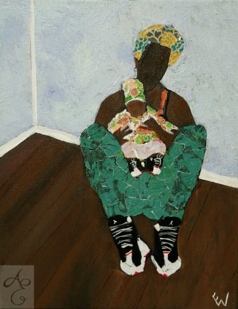 May include: A woman wearing a green and black patterned outfit and a floral headband holds a baby wearing a pink and floral dress. The woman is sitting on a wooden floor with her legs crossed. The woman and baby are in a corner of a room with a light blue wall.