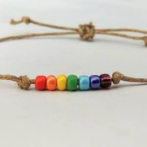 May include: A rainbow-colored beaded bracelet with a brown cord. The beads are red, orange, yellow, green, blue, and purple.