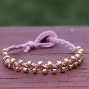 May include: A pink braided bracelet with gold beads. The bracelet is tied with a knot at the end.