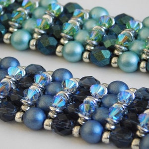 Puede incluir: Un brazalete de múltiples hilos con cuentas azules y verdes. El brazalete está hecho con una variedad de cuentas, incluyendo cuentas redondas, facetadas y de cristal. Las cuentas están dispuestas en un patrón repetitivo.