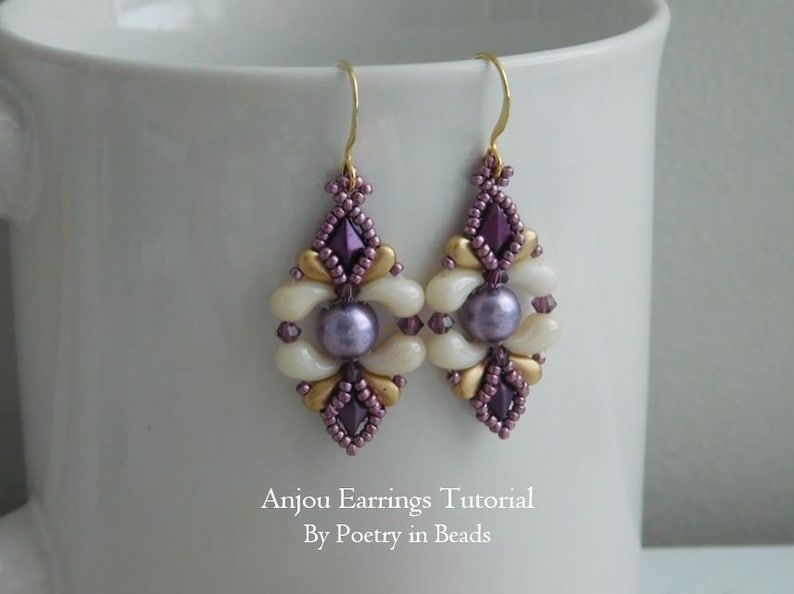 Puede incluir: Un par de pendientes de cuentas moradas y blancas con detalles dorados. Los pendientes tienen forma de diamante y presentan una gran perla en el centro. Los pendientes cuelgan de ganchos dorados. El texto "Anjou Earrings Tutorial By Poetry in Beads" es visible debajo de los pendientes.