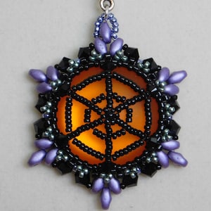 Puede incluir: Un colgante de cuentas con un diseño de telaraña negra sobre un fondo naranja. El colgante está rodeado de cuentas moradas y negras.