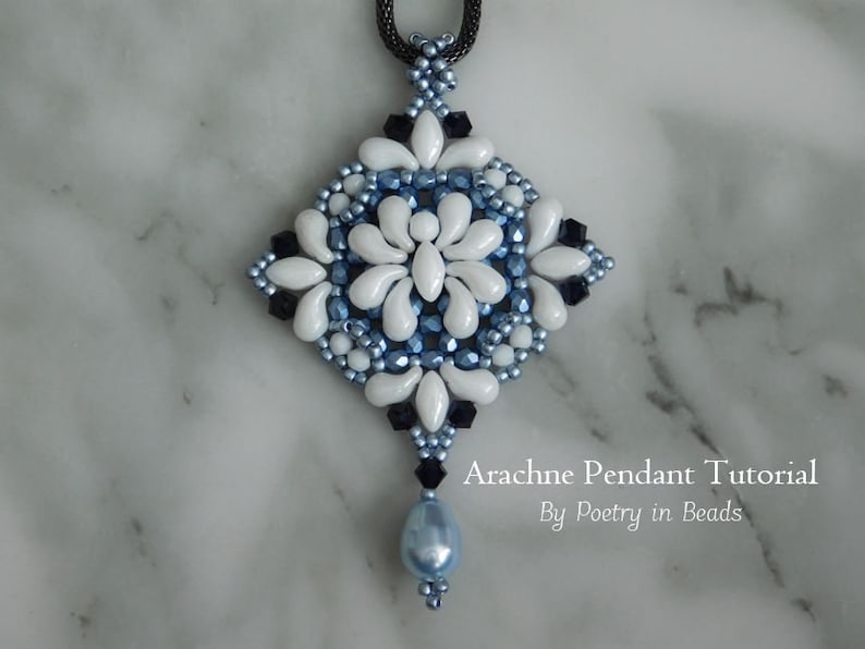 K&ouml;nnte beinhalten: Ein wei&szlig;er und blauer Perlenanh&auml;nger mit einem schwarzen Perlen-Tropfen, der ein geometrisches Design aufweist. Der Anh&auml;nger befindet sich auf einer wei&szlig;en Marmorfl&auml;che. Arachne Pendant Tutorial by Poetry in Beads.