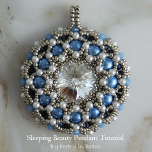 May include: A silver and blue beaded pendant with a clear crystal in the centre. The pendant is round and has a delicate design. The text "Sleeping Beauty Pendant Tutorial By Poetry in Beads" is at the bottom of the image.
