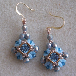 May include: A pair of dangle earrings with a blue and silver bead design. The earrings feature a square-shaped cluster of beads with a larger blue bead in the center.