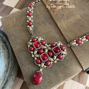 May include: A red and gold beaded necklace with a heart-shaped pendant and a teardrop-shaped bead. The necklace is on a brown leather surface. Troubadour Necklace Tutorial by Poetry in Beads.