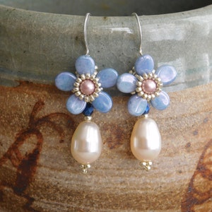 May include: A pair of dangle earrings featuring a blue flower design with a pearl drop. The flower is made of blue and pink beads and has a silver wire.
