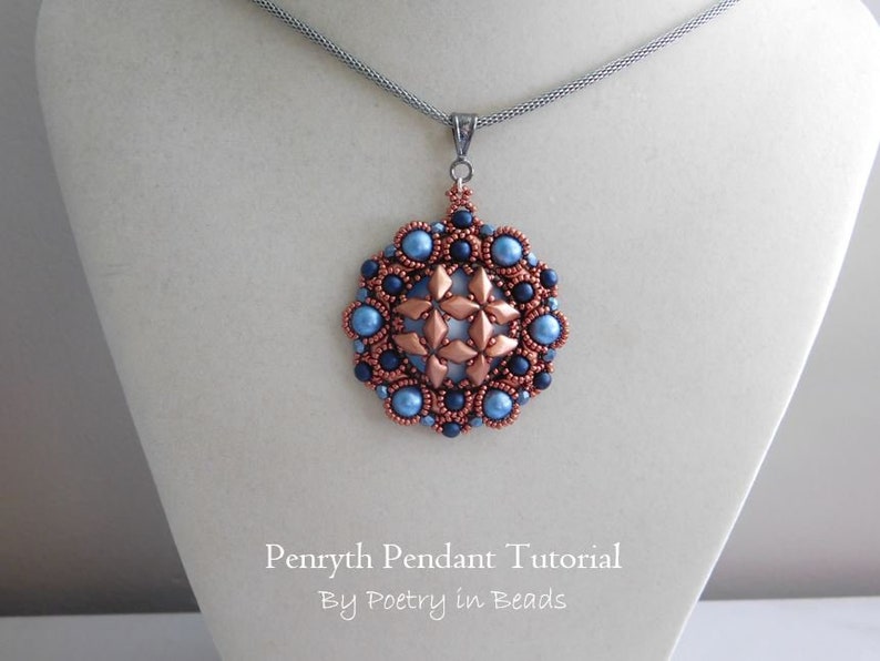 Puede incluir: Un collar con un colgante de cuentas de cobre y azul con un dise&ntilde;o de estrella. El colgante cuelga de una cadena plateada en un expositor blanco. El texto "Pennyrth Pendant Tutorial By Poetry in Beads" est&aacute; debajo del colgante.
