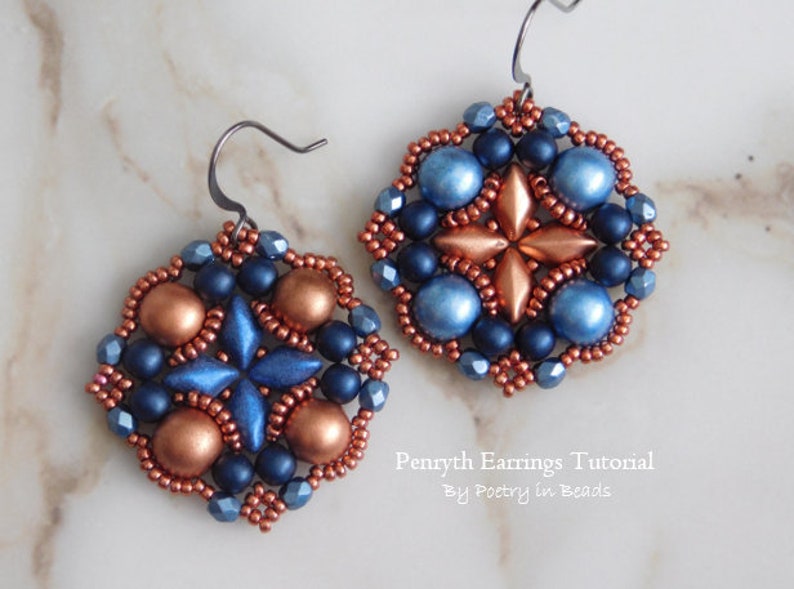 May include: A pair of copper and blue beaded earrings with a starburst design. The earrings are made with small seed beads and larger round beads. The earrings are hanging from silver hooks.
