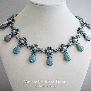 May include: A beaded necklace with a silver and blue colour scheme. The necklace features a series of teardrop-shaped beads and a central row of round beads. The necklace is displayed on a white mannequin. The text "L'Amore Necklace Tutorial by Poetry in Beads" is displayed below the necklace.