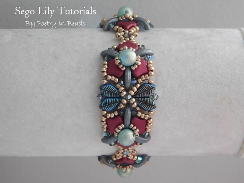 May include: A beaded bracelet with a repeating pattern of burgundy, blue, and gold beads. The bracelet is on a white surface.