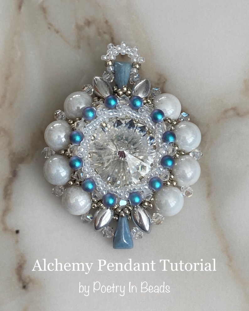 Pode incluir: Um pingente de contas prateadas e azuis com um cristal transparente no centro. O pingente &eacute; rodeado por contas brancas e tem um la&ccedil;o prateado no topo. O pingente est&aacute; sobre um fundo de m&aacute;rmore branco. Alchemy Pendant Tutorial by Poetry In Beads.