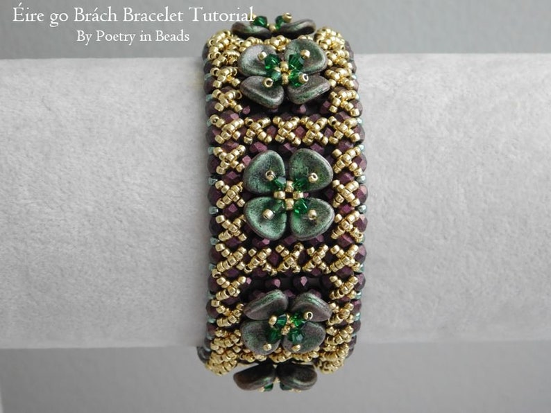 Pu&ograve; includere: Un braccialetto di perline con uno schema di colori oro e viola. Il braccialetto presenta tre ciondoli a forma di fiore verde con accenti di cristallo verde. Il braccialetto &egrave; intitolato "&Eacute;ire go Br&aacute;ch Bracelet Tutorial By Poetry in Beads".