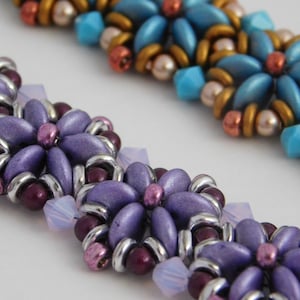 Op de afbeelding: Close-up van een paarse en zilveren kralen armband met een bloemenpatroon. De armband is gemaakt met kleine, ronde kralen en heeft een delicate, vrouwelijke uitstraling.