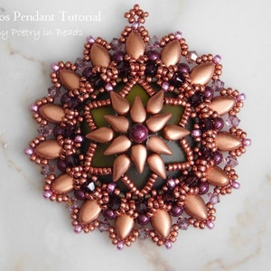 May include: A copper and purple beaded pendant with a starburst design. The pendant is made with seed beads and larger teardrop-shaped beads. The pendant is on a white marble surface.