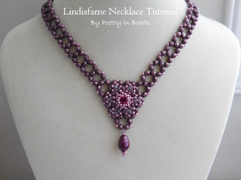 May include: A purple and pink beaded necklace with a flower pendant and a single drop bead. The necklace is on a white mannequin bust. The text "Lindisfarne Necklace Tutorial By Poetry in Beads" is above the necklace.