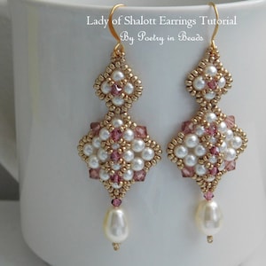 Op de afbeelding: Een paar gouden oorbellen met witte parels en roze kristallen. De oorbellen hebben de vorm van een diamant met een hangende parel aan de onderkant. De oorbellen worden "Lady of Shalott Earrings" genoemd en zijn van "Poetry in Beads".