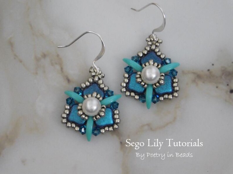 May include: A pair of silver earrings with a blue and turquoise flower design and a white pearl in the center. The earrings are on a white marble surface. Sego Lily Tutorials by Poetry in Beads.