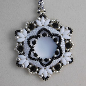 May include: A white and black beaded snowflake earring with a silver loop. The snowflake has a central circle with black beads around the edge.