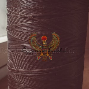 May include: A spool of brown waxed thread with a gold and blue Egyptian winged sun logo.