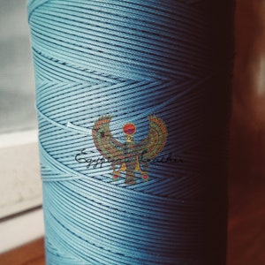 May include: A spool of light blue cotton cord with the text "Egyptian Leather" and a stylized image of a winged sun god.