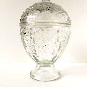 May include: A clear glass candy dish with a domed lid. The dish has a pedestal base and is decorated with a floral pattern.