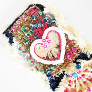 Sacred Heart textile art brooch embellished with upcycled fabrics. polymer clay mini flowers, glass beads and colorful embroidery floss.