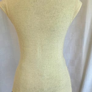 Puede incluir: Top de punto amarillo p&aacute;lido con cuello redondo y mangas cortas. El top ajustado se muestra en un maniqu&iacute;, mostrando su silueta ajustada. La tela parece suave y ligeramente texturizada, sugiriendo un uso c&oacute;modo.