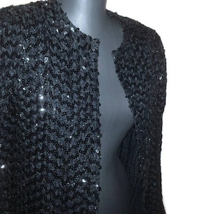 May include: A black sequined jacket with a long sleeve and a zip closure.