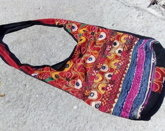Puede incluir: Una bolsa de tela roja, negra, azul y amarilla bordada con una correa larga. La bolsa está decorada con motivos florales y cuentas de colores.