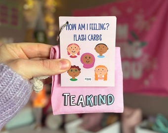 May include: Pink and white flash cards with the title "How Am I Feeling? Flash Cards" and illustrations of different faces. The cards are folded and held in a hand. The cards have the hashtag #TeaKind printed on them.