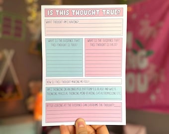 May include: A white and pink notepad with the text "IS THIS THOUGHT TRUE?" and prompts for self-reflection. The notepad includes sections for identifying thoughts, evidence, and reframing. The notepad is held by a hand.