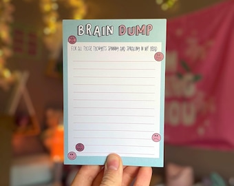 May include: A blue and pink notepad with the text "BRAIN DUMP" and the phrase "FOR ALL THOSE THOUGHTS SPINNING AND SPIRALLING IN MY HEAD". The notepad has lined paper and pink smiley faces.