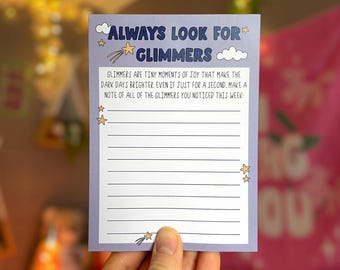 May include: A light purple notepad with the text "ALWAYS LOOK FOR GLIMMERS" and lined spaces for writing. The notepad has star and cloud illustrations. The text reads: "Glimmers are tiny moments of joy that make the dark days brighter."