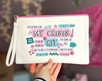 May include: White canvas pouch with a pink zipper and pink trim. The pouch has a colorful graphic design with the text "My Crisis Kit" and phrases like "You are never alone", "You are not a burden", "You will get through this", "Your feelings are valid", "You are so loved", and "You are brave".
