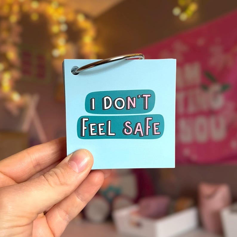 May include: A square light blue card held by a metal ring. The card features a dark teal horizontal graphic with the text "I DON'T FEEL SAFE" printed in white and pink letters. The card is made of smooth paper and has a clean, matte finish.