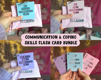 May include: A bundle of communication and coping skills flash cards. The cards are in various colors, including blue, pink, and purple, and are held in small pink pouches. The text on the cards includes "My Feelings Communication Cards" and "My Needs Communication Cards."