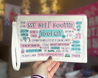 May include: A white canvas zippered pouch with a pink and blue design. The pouch has the words "My Self Soothe Toolkit" printed on it. The pouch is filled with positive affirmations and encouraging messages.