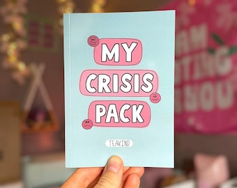 May include: A light blue card with the text "MY CRISIS PACK" in pink bubble letters. The card has a sad face, a worried face, and an angry face. The word "TEAKIND" is at the bottom of the card.