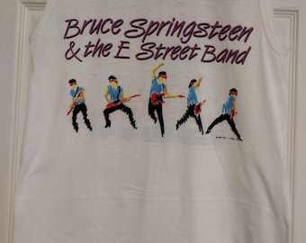 May include: White sleeveless t-shirt with a pink and black graphic of Bruce Springsteen and the E Street Band. The band members are depicted in a pixelated style playing guitars.