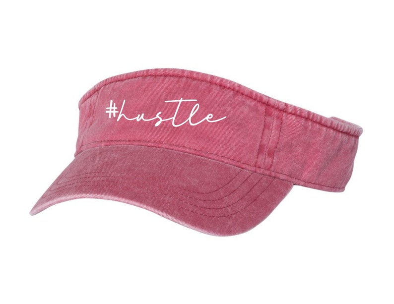 May include: A red, distressed, cotton visor with a white embroidered hashtag and the word "hustle".