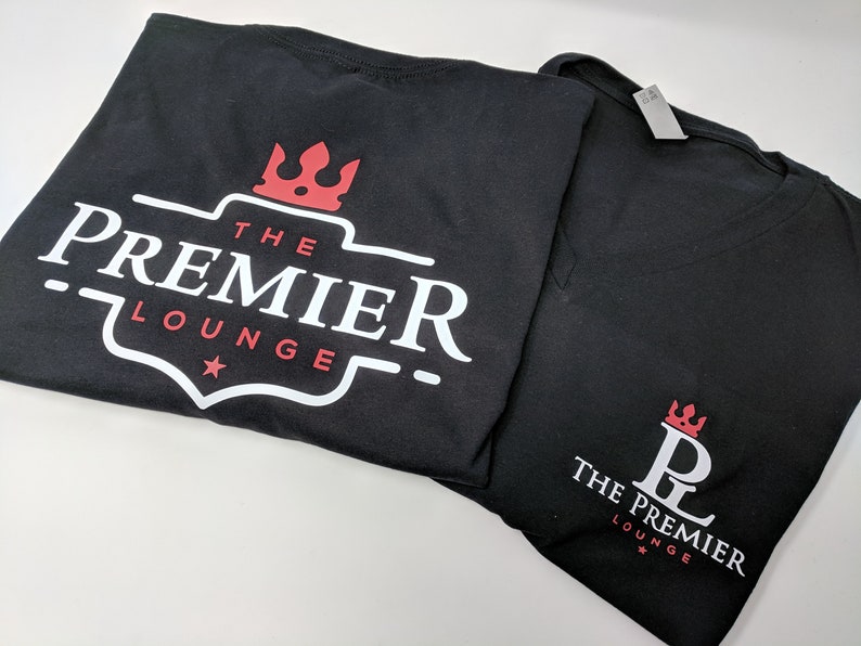Pu&ograve; includere: Due magliette nere con un logo bianco che dice "The Premier Lounge" e una corona rossa. Una maglietta ha un logo pi&ugrave; grande con una stella e l'altra ha un logo pi&ugrave; piccolo con un "PL" stilizzato al centro.