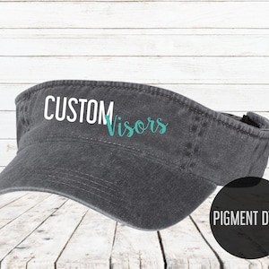 May include: A gray pigment dyed visor with the text "CUSTOM Visors" in white and teal lettering.