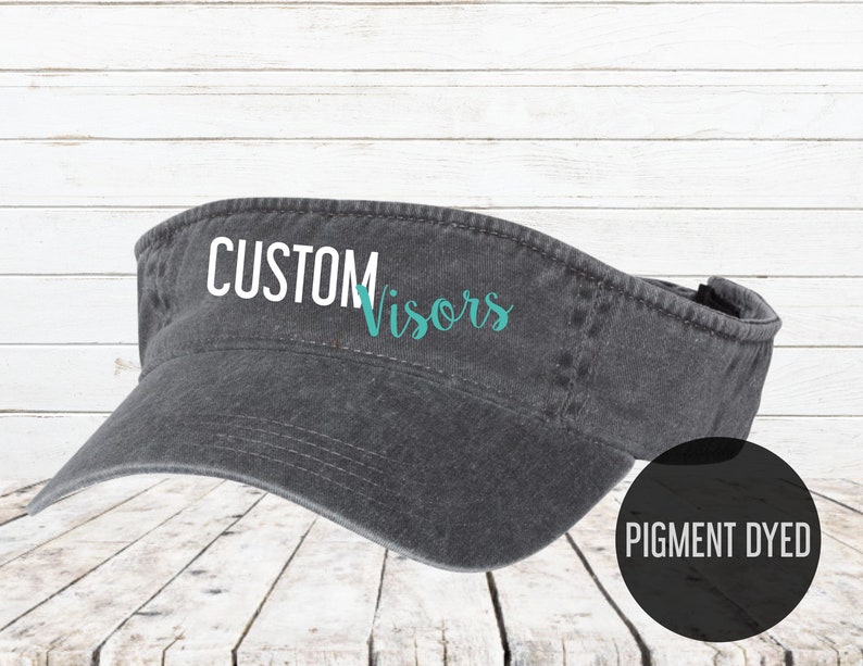 May include: A gray pigment dyed visor with the text "CUSTOM Visors" in white and teal lettering.