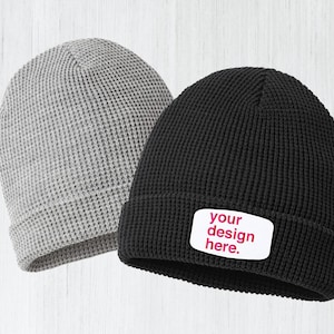 May include: Two knit beanies, one gray and one black, with a white patch on the black beanie that says "your design here".