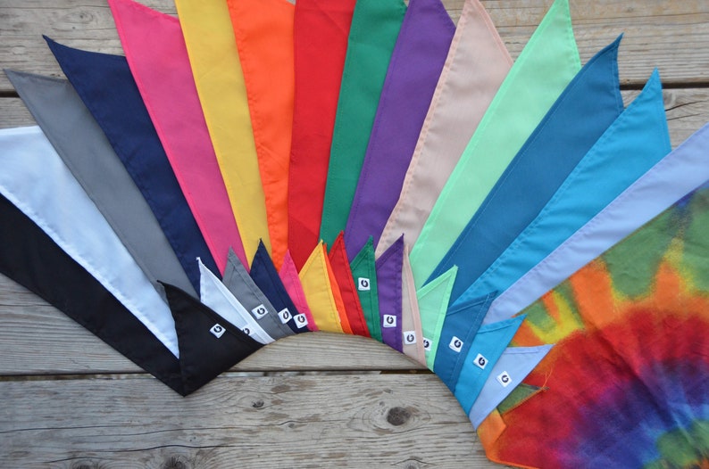 May include: A collection of 17 colorful fabric bandanas arranged in a fan shape. The bandanas are in various colors, including white, black, gray, pink, yellow, orange, red, green, purple, beige, light blue, dark blue, and light purple. The bandanas are all folded in a triangular shape and have a small white tag with a number on it.