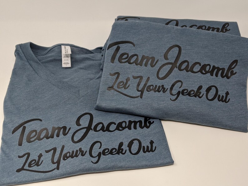 May include: Three blue t-shirts with a black graphic that says "Team Jacomb Let Your Geek Out".