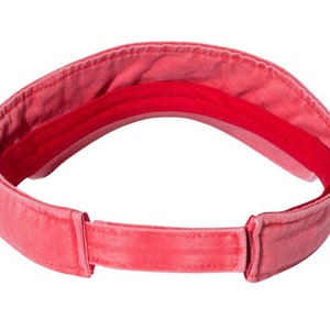 May include: A red visor made of cotton with a fabric strap. The visor is designed to protect the eyes from the sun.