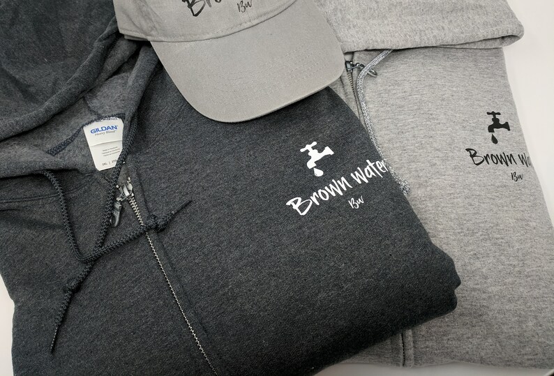 May include: Two hooded sweatshirts with a zipper closure. The sweatshirts are gray and dark gray. Both sweatshirts have a white logo with a faucet and the text "Brown Water Brew". A gray baseball cap with the same logo is also pictured.