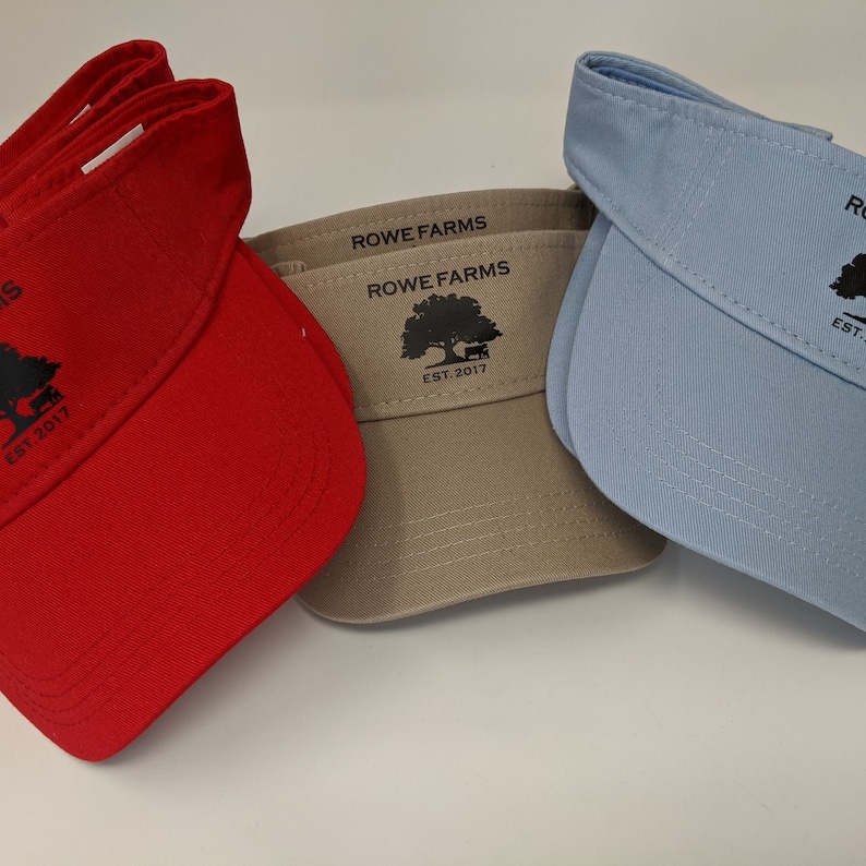 May include: Three visors with the text "Rowe Farms Est. 2017" and a tree logo. The visors are red, beige, and light blue.